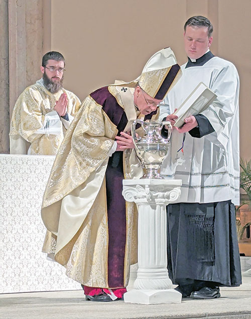 Archbishop Charles C. Thompson ritually breathes on chrism oil on March 26 during the annual archdiocesan chrism Mass at SS. Peter and Paul Cathedral in Indianapolis. Assisting at the Mass are transitional Deacon Bobby Vogel, left, and seminarian Samuel Hansen. (Photo by Sean Gallagher)