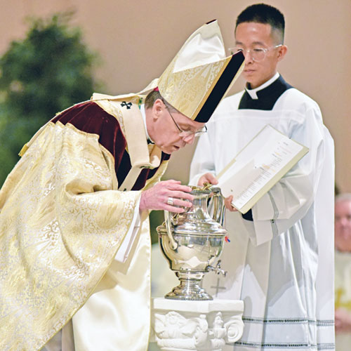 Archbishop Charles C. Thompson ritually breathes upon chrism oil on April 15 during the annual archdiocesan chrism Mass at SS. Peter and Paul Cathedral. Seminarian Khaing Thu, right, assists at the Mass. (Photo by Sean Gallagher)