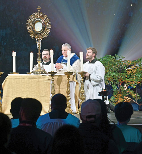 Father Liam Hosty, left, U.S. Military Services Archbishop Timothy P. Broglio and seminarian Lucas LaRosa kneel in adoration before Christ in the Blessed Sacrament in Lucas Oil Stadium in Indianapolis on Nov. 21 during the National Catholic Youth Conference. (Photo by Natalie Hoefer)