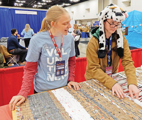 Volunteer Kelli Reutman of Catalyst Catholic in the New Albany Deanery, left, supervises Sela Kubiak of the Archdiocese of Detroit as she helps make a mat for the homeless by taking plastic bags and weaving them together. (Photo by Mike Krokos)