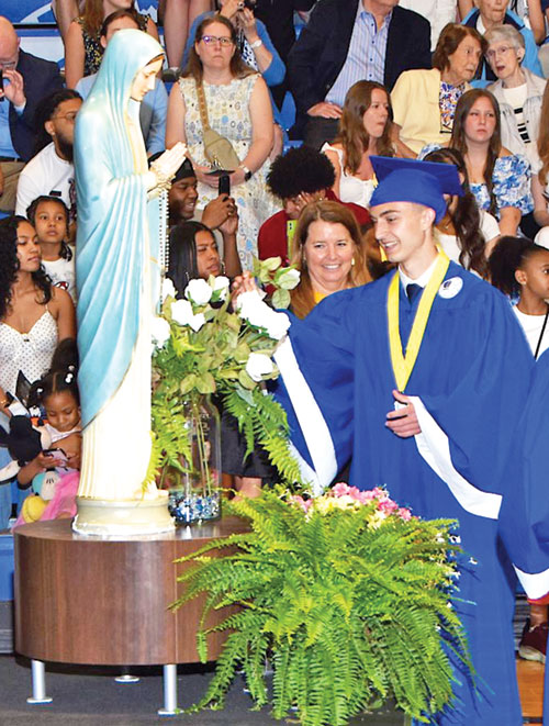 As part of the graduation tradition at Bishop Chatard High School in Indianapolis, a number of seniors place a rose at the foot of a statue of the Blessed Mother during the procession at the beginning of the commencement ceremony. J.D. Haines places his rose in honor of Mary during the school&rsquo;s 2025 graduation. (Submitted photo)