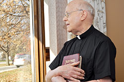 Father Herman Lutz looks out of a parlor window at St. Paul Hermitage in Beech Grove in this Nov. 27, 2013, photo. The Hermitage is home to Father Lutz, who still ministers to the residents of the Hermitage and the Altenheim Community despite being retired. (Photo courtesy of the archdiocesan Office of Stewardship and Development)