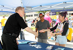 Father Rick Ginther, left, director of the archdiocesan Office of Ecumenism and pastor of St. Patrick and St. Margaret Mary parishes, both in Terre Haute, greets visitors to his table representing the archdiocesan Office of Ecumenism at the Festival of Faiths in Indianapolis on Aug. 30. (Photo by Natalie Hoefer)