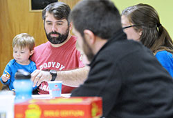 Ryan Raelson holds his son Sawyer while playing Apples to Apples Bible Edition with his wife Sarah (partially obscured) and seminarian Michael Bower during a family game night at Holy Name Parish in New Albany on March 2. (Photo by Natalie Hoefer)
