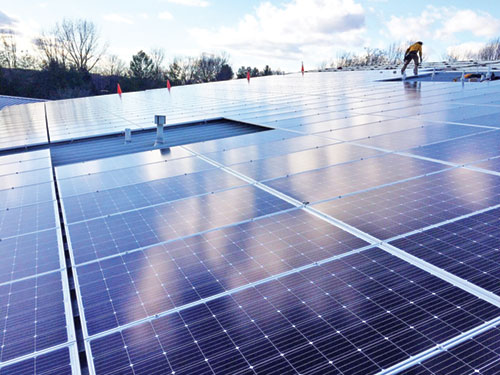 New solar panels gleam on the roof of the Parish Life Center at St. John the Apostle Parish in Bloomington as a workman installs the final panels on Dec. 6, 2017. (Photo courtesy of Cliff Burk)