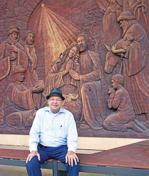 Andy Hohman, a retired philosophy and theology professor at Marian University in Indianapolis, sits by a relief sculpture of the adoration of the Magi on its campus on July 30. He recently retired after spending 40 years on the university’s faculty. (Photo by Sean Gallagher)