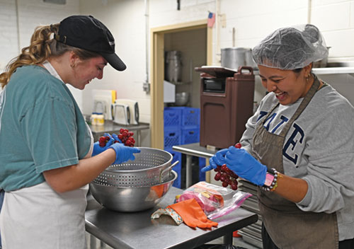 Therese Hauersperger, left, a member of the college student organization of St. John the Evangelist Parish in Indianapolis, and Leslie Venegas, a Fellowship of Christian University Students&rsquo; missionary at the parish, prepare food on Oct. 9 for the Cathedral Kitchen in Indianapolis. On Nov. 8, an open house and blessing will highlight recent Cathedral Kitchen restorations, including upgrades to electrical, plumbing and structural systems. (Photo by Emily Mastronicola)