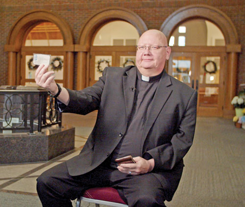 Father John McCaslin, pastor of St. Monica Parish in Indianapolis, shows a business card with the archdiocesan vocations director’s contact information he received 30 years ago that was a pivotal moment in his discernment of his vocation to the priesthood. He’s kept the business card as a “sign of God’s faithfulness to me.” (Photo courtesy of Cantaloupe)