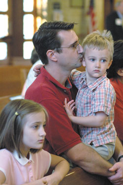 Jeff Ellenberger of New Palestine kisses his son, Nathan, while his daughter, Claire, kneels beside them during the Mass of Thanksgiving for St. Theodora. Jeff and Patricia Ellenberger and their five children are members of St. Michael Parish in Greenfield.