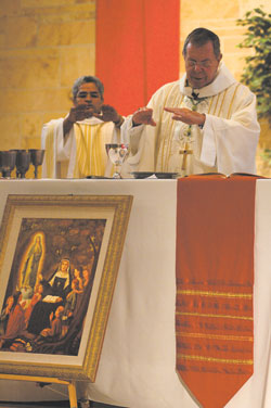 Archbishop Daniel M. Buechlein and Father Varghese Maliakkal, administrator of St. Michael the Archangel Parish, consecrate the Eucharist during a Sept. 29 feast day Mass at the Indianapolis West Deanery church. A nine-day novena preceded the liturgy. The portrait depicting St. Theodora Guérin teaching children will hang on a pillar in the church.	