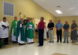 Archbishop Daniel M. Buechlein is presented with a plaque during the Sept. 16 dedication of the new parish life center at St. John the Baptist Parish in Dover. Standing in front of the archbishop is parishioner Jim Hountz, chairman of the facility’s building committee. Other members of the committee standing to the side are, from left, Ed Graf, Jamie Graf, Gary Gaynor and Joan Brewer. Standing behind the archbishop are, from left, Ford Cox, master of ceremonies for episcopal ­celebrations, and Father Joseph Feltz, dean of the Batesville Deanery. Father George Plaster, pastor of St. John the Baptist Parish, stands to the archbiship’s left. The plaque ­recognized the committee and the dedication of the parish life center.