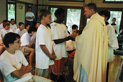 Father Rick Nagel, associate vocations director for the archdiocese, receives offertory gifts from, at left, Patrick Durcholz, a member of Annunciation Parish in Brazil, and Kevin Chambers, a member of Holy Trinity Parish in Indianapolis, during a Mass celebrated on June 14 at Bradford Woods in Morgan County. The Mass was part of Bishop Bruté Days, a retreat focused on the priesthood that was sponsored by the Bishop Bruté College Seminary at Marian College in Indianapolis. (File photo/Sean Gallagher) 