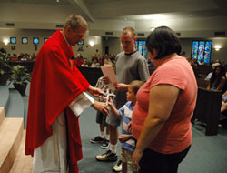 Father Rick Nagel presents a crucifix to Joshua Brown during a Sept. 14 Mass celebrated at Our Lady of the Greenwood Church in Greenwood during the opening weekend of the Parish Vocations Cross Initiative. Joshua received the crucifix on behalf of his parents, Jennifer and Brian Brown, and his brother, Marcus. The cross initiative is sponsored by the archdiocesan Office of Priestly and Religious Vocations. Father Nagel is Our Lady of the Greenwood’s associate pastor and the associate director of archdiocesan vocations. (Photo by Sean Gallagher) 