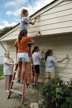 Senior citizen Pansy Mitchell of Indianapolis watches members of Roncalli High School’s varsity volleyball team paint her faded garage on Sept. 27 during the ninth annual Angels from the Heart community service project coordinated by Sacred Heart of Jesus Parish. The service program was organized in 2000 to celebrate the 125th anniversary of the founding of Sacred Heart Parish in 1875 on the near-south side of the city. (Photo by Mary Ann Wyand) 