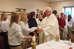 Father James Wilmoth, chaplain of Roncalli High School and pastor of St. Roch Parish, both in Indianapolis, gives the sign of peace to Audrey Meyers, a Roncalli sophomore who is a member of Holy Name of Jesus Parish in Beech Grove, during a Nov. 12 Mass at the school. Waiting to give the sign of peace to Father Wilmoth is Roncalli sophomore Meg Naumovich, a member of Our Lady of the Greenwood Parish in Greenwood. (Photo by Sean Gallagher) 
