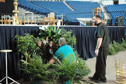Father Aaron Jenkins works on art and environment details for the stage on May 2 at Lucas Oil Stadium in Indianapolis in preparation for the archdiocese’s 175th anniversary Mass there on May 3. He is the associate pastor of Holy Name of Jesus Parish in Beech Grove and the chaplain of Father Thomas Scecina Memorial High School in Indianapolis. A group of Scecina Memorial students helped him move the liturgical furniture onto the stage. (Photo by Mary Ann Wyand) 