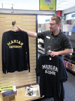 Zack Fincher, Marian University Bookstore supervisor, removes the last three T-shirts with “Marian College” printed on them and replaces them with “Marian University” T-shirts. All “Marian College” items were on sale for 75 percent off the original price. “These [Marian College T-shirts] are pretty much all that’s left,” Fincher said. (Photo by Kamilla Benko) 