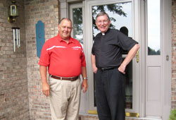 Frank Wiseman Jr. and Father Michael Hilderbrand, pastor of St. Mary Parish in Lanesville, stand together in front of Wiseman’s house in Floyds Knobs on July 30. The house is built on the same site where, 19 years ago, Wiseman’s previous house was destroyed by a tornado. Later that same day, Father Hilderbrand prayed with Wiseman, a member of St. Mary-of-the-Knobs Parish in Floyd County, and helped him contact family members who were away from home. (Submitted photo)
