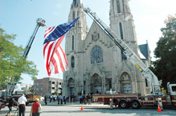 A giant American flag is held aloft from the ladders of two fire trucks parked in front of St. Mary Church in Indianapolis on Sept. 11 before a Mass celebrated to honor the service of all emergency responders, and especially those who lost their lives responding to the terrorist attacks on Sept. 11, 2001, in New York and Washington, D.C. (Photo by Sean Gallagher)
