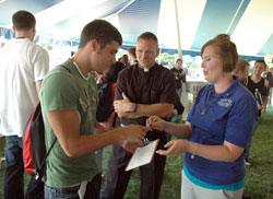 Alexandra Kale, right, hands a survey to Indiana University-Purdue University Indianapolis (IUPUI) student Ryan Burke of Elwood, Ind., during an activities fair on the university campus on Sept. 1 while Father Rick Nagel, IUPUI chaplain, looks on. Kale and three other recent college graduates are missionaries to IUPUI from the Fellowship of Catholic University Students (FOCUS). They are joining Father Nagel, Echo apprentice Joe Pedersen and a handful of Catholic IUPUI students in renewing Catholic campus ministry for the 30,000 IUPUI students. (Photo by Sean Gallagher)