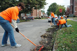 Kitty Fischer, at left, the parish council president at St. Matthew the Apostle Parish in Indianapolis, rakes weeds and dirt away from a curb on Oct. 3 near Holy Trinity Church in the Indianapolis West Deanery. She was among more than 400 volunteers who helped clean some of the streets in the near west side neighborhood as part of the Parish Partners volunteer effort with St. Barnabas, St. Anthony and Holy Trinity parishioners of all ages. (Photo by Mary Ann Wyand)