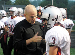 After a play during a football game against Park Tuder School on Sept. 25, Father John Hollowell shares a coaching moment with Eddie Cmehil, a sophomore wide receiver and defensive back for Cardinal Ritter’s varsity football team. (Photo by John Shaughnessy)