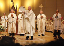During the Dec. 9 episcopal ordination and installation of Bishop Paul D. Etienne in the Cheyenne Civic Center in Cheyenne, Wyo., Father Michael Carr, vicar general of the Cheyenne Diocese, holds the apostolic letter from Pope Benedict XVI in which the pontiff appointed Bishop Etienne to lead the Church in Wyoming. Standing behind Father Carr applauding are Fathers Carl Gallinger, left, James Heiser and Thomas Cronkleton, all priests of the Cheyenne Diocese and members of its college of consultors. (Photo by Sean Gallagher)