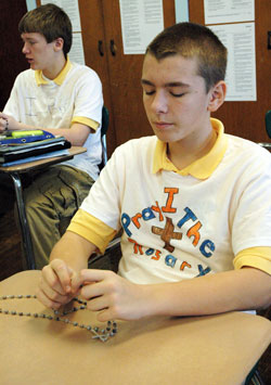 Holy Name School eighth-grade students Ben Coons, right, and Jake Farnworth, left, of Beech Grove pray a decade of the rosary on Jan. 13 during religion class. Ben, Jake and other classmates recently decorated T-shirts with the message “I pray the rosary” to promote their Catholic faith as well as their devotion to Jesus and Mary. (Photo by Mary Ann Wyand)