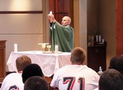 Father John Hollowell celebrates Mass on Sept. 25, 2009, for members of the varsity football team of Cardinal Ritter Jr./Sr. High School in Indianapolis. As a chaplain, teacher and assistant football coach at Cardinal Ritter, Father Hollowell celebrates Mass on the Friday afternoon before every football game—continuing the emphasis that head coach Ty Hunt has of making faith a crucial part of the teenagers’ football experience. (Photo by John Shaughnessy)