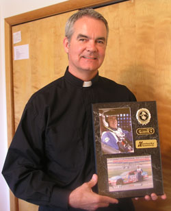 Standing in his office, Father John Meyer holds a plaque that celebrates one of the most unusual adventures that he’s had during his 28 years as a priest in the archdiocese—driving up to 150 mph at the Kentucky Speedway while participating in the Richard Petty Driving School. The experience was a gift from one of the two parishes he leads in southern Indiana. (Photo by John Shaughnessy)
