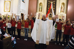 Franciscan Father Arturo Ocampo, pastor of St. Patrick Parish in Indianapolis, sings with youths and young adults involved in Las Jornadas, a Hispanic lay movement in the Church, at the start of an April 18 Mass at his parish’s church. (Photo by Sean Gallagher)