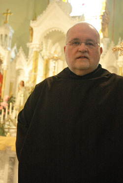 Benedictine Father Barnabas Gillespie stands in front of the altar at St. Pius V Church in Troy. He serves as the pastor of that parish and St. Michael Parish in Cannelton, and provides sacramental assistance at St. Paul Parish in Tell City and St. Mark Parish in Perry County. (Photo by Sean Gallagher)
