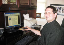 Father Eric Augenstein, pastor of Our Lady of Perpetual Help Parish in New Albany, sits at his computer in the parish office on July 7. On his blog, “Perpetual Priest,” Father Augenstein posts the text of his weekend homilies, thus widening the reach of his ministry. (Submitted photo)