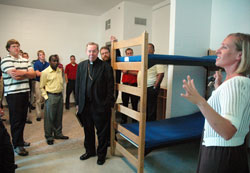 Emily Able, director of community and youth services at Holy Family Shelter in Indianapolis, guides Archbishop Daniel M. Buechlein, center, archdiocesan vocations director Father Eric Johnson, standing behind the archbishop, and a group of archdiocesan seminarians on an Aug. 11 tour of the homeless shelter. (Photo by Sean Gallagher)