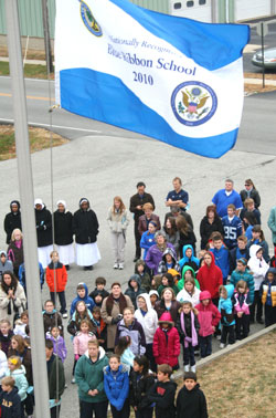 Students of Our Lady of the Greenwood School raise a special flag proclaiming it a Blue Ribbon School of Excellence during a Nov. 19 ceremony with staff members. (Photos by Tony Cooper)