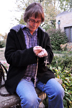 Our Lady of Lourdes parishioner Linda Abner of Indianapolis prays the rosary at the Marian grotto adjacent to Our Lady of Lourdes Church last fall. Members of the parish Spiritual Life and Worship Commission and rosary group organize regular rosary times for parishioners and Our Lady of Lourdes School students. (Photo by Mary Ann Wyand)