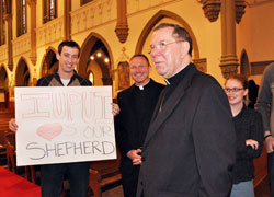 Archbishop Daniel M. Buechlein talks with Indiana University-Purdue University Indianapolis senior Michael Conner, left, of St. Paul Parish in Tell City, who holds a sign praising Archbishop Buechlein after the Jan. 14 press conference at St. John the Evangelist Church in Indianapolis. Father Rick Nagel, center, the director of the archdiocesan Office of Young Adult and College Campus Ministry, also talked with the archbishop and students after Bishop-designate Christopher J. Coyne’s official introduction. (Photo by Mary Ann Wyand)