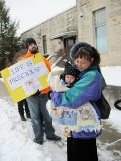 Cindy Lee holds her 5-month-old son, Simon, as she prays outside the Planned Parenthood clinic in Bloomington during the March for Life on Jan. 24. They are members of St. Paul Catholic Center in Bloomington. Holding the poster is Patrick Faulkenberg, a member of St. John the Apostle Parish. (Photo by Kamilla Benko)