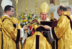 Archbishop Daniel M. Buechlein prays over Bishop-designate Christopher J. Coyne as transitional Deacon Dustin Boehm of Greenwood, left, and Deacon Joseph Holderried of St. Margaret Mary Parish in Westwood, Mass., hold a Book of Gospels over the new auxiliary bishop’s head on March 2 at St. John the Evangelist Church in Indianapolis. This part of the ordination is a sign that the faithful preaching of the word of God is the pre-eminent obligation of the office of the bishop. (Photo by Mary Ann Wyand)
