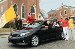 Father Jonathan Meyer, pastor of St. Mary, St. Ann and St. Joseph parishes in Jennings County, sits behind the wheel of his 2009 Toyota Corolla, which he is giving away to raise funds to help nine young adults attend World Youth Day on Aug. 16-21 in Madrid, Spain. Six young adults from Jennings County parishes posing with Father Meyer to promote the fundraiser are, from left, Danny Capes, Kelly Ertel, Charlotte Leach, Amber Andrews, Laura Coons and Kate Eder. Capes, Ertel, Leach, Coons and Eder are among the World Youth Day pilgrims. (Submitted photo)