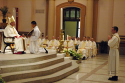 During the June 4 ordination Mass at SS. Peter and Paul Cathedral in Indianapolis, several priests look on as Bishop Christopher J. Coyne, left, auxiliary bishop and vicar general, asks questions of transitional Deacon Dustin Boehm, right, to determine if he is willing to carry out the duties of the priesthood. Assisting Bishop Coyne is seminarian Martin Rodriguez. (Photo by Sean Gallagher)