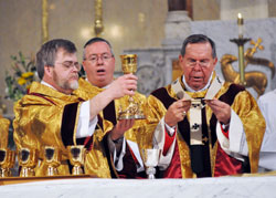Assisting Archbishop Daniel M. Buechlein, right, Deacon Kerry Blandford, left, elevates the chalice during the doxology of the eucharistic prayer during the March 2 episcopal ordination of Bishop Christopher J. Coyne, center, at St. John the Evangelist Church in Indianapolis. (File photo by Mary Ann Wyand)