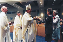 Archbishop Daniel M. Buechlein accepts offertory gifts from Beverly Hansberry and Franciscan Sister Yvonne Conrad at the Dec. 1, 2001, dedication Mass for the new St. Simon the Apostle Church in Indianapolis. Transitional Deacon John McCaslin, left, a St. Simon parishioner who was ordained to the priesthood in June 2002, and Father Robert Sims, then St. Simon’s pastor, assisted the archbishop during the liturgy. At the time, Hansberry was St. Simon’s director of faith formation, and Sister Yvonne was the parish’s administrative assistant. (File photo by Mary Ann Wyand)
