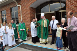 Bishop Christopher J. Coyne, center, auxiliary bishop and vicar general, blesses the new St. Anne Parish Center during a dedication ceremony on Aug. 14 in New Castle. Assisting the bishop are, from left, altar servers Timmy Welch and Margy Welch; Father Joseph Rautenberg, sacramental minister; Father Stanley Herber, dean of the Connersville Deanery and priest moderator; Ford Cox, executive assistant to the archbishop and auxiliary bishop and liaison for episcopal affairs; lifetime parishioner John McGrady; parishioner Brittany West; longtime parishioner Iris Niflis; and deacon candidate Russell Woodard, parish life coordinator. (Photo by Mary Ann Garber)