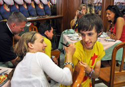One of the many fun things about World Youth Day is connecting with people from other countries. Dana Petricka, left, a member of St. John the Evangelist Parish in Indianapolis, signs the shirt of a young pilgrim from Paris, France. Behind her, Father Rick Nagel, director of the archdiocesan Office of Young Adult and College Campus Ministry, Catholic chaplain at Indiana University-Purdue University Indianapolis (IUPUI), and administrator of St. John the Evangelist Parish in Indianapolis, signs the shirt of another pilgrim. (Photo by Megan Fish)