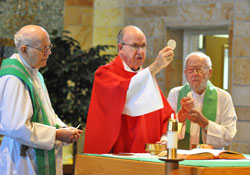 Father Gerald Burkert, center, elevates the Body of Christ during a Sept. 25 Mass at the chapel of St. Paul Hermitage in Beech Grove, where he is a resident and chaplain. Concelebrating the Mass with him are, from left, Father Herman Lutz and Father Elmer Burwinkel, who are also residents at St. Paul Hermitage. (Photo by Sean Gallagher)