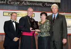 Bishop Christopher J. Coyne presents an award for Archbishop Emeritus Daniel M. Buechlein to his niece, Anne Wilmes, during the Celebrating Catholic School Values Awards Dinner on Oct. 26. The award recognized the archbishop for making Catholic education a priority during his 19-year tenure as the spiritual leader of the archdiocese. The archbishop was unable to attend the dinner. Also in the photo are, left, Harry Plummer, executive director of Catholic education and faith formation for the archdiocese, and Art Wilmes, Anne’s husband. (Photo by Rob Banayote)