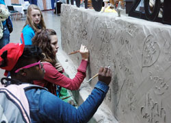 Tierra Scott, front, and Savannah Burton carve their names into a wall made of 2,000 pounds of clay in the Creative Corner section of Victory Park, a theme park of fun and faith at the National Catholic Youth Conference in Indianapolis on Nov. 17. The teenagers are members of Holy Trinity Parish in Glenburnie, Md., in the Archdiocese of Baltimore. (Photo by John Shaughnessy)