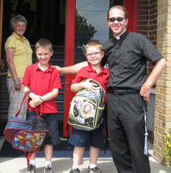 Matthew Graf, left, and his brother, Nathan, pose for a picture at St. Paul School in New Alsace with Father Scott Nobbe, who is both the parish priest and the principal of the school. School secretary Millie Kraus watches in the background. (Submitted photo)