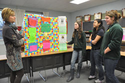 Jill Mires, left, principal of Pope John XXIII School in Madison, speaks with sixth-grade students Summer Martin, Leigh Ann Gaminde and Erin Cooper on Jan. 11 about a presentation board created for the CLASS (“Connecting Learning Assures Successful Students”) program. (Photo by Sean Gallagher)
